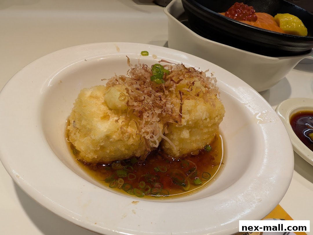 A close-up of crispy fried tofu topped with bonito flakes and green onions in a savory sauce.
