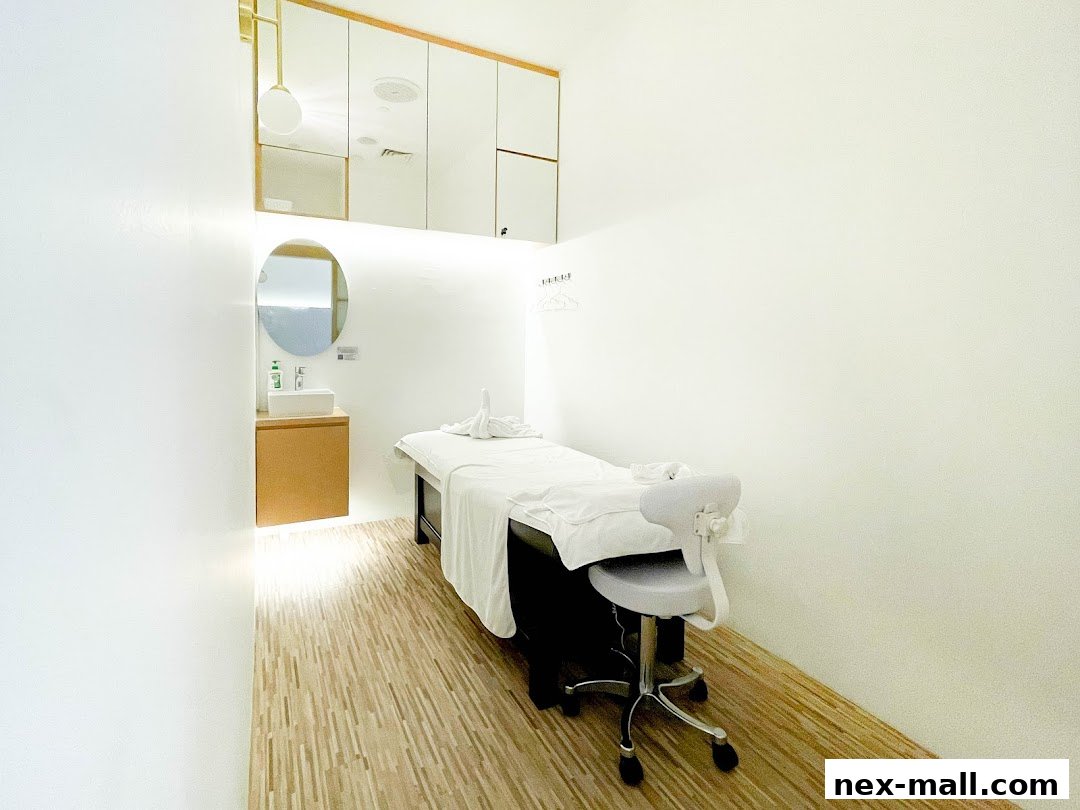 A clean and modern treatment room with a massage bed, chair, and sink area.