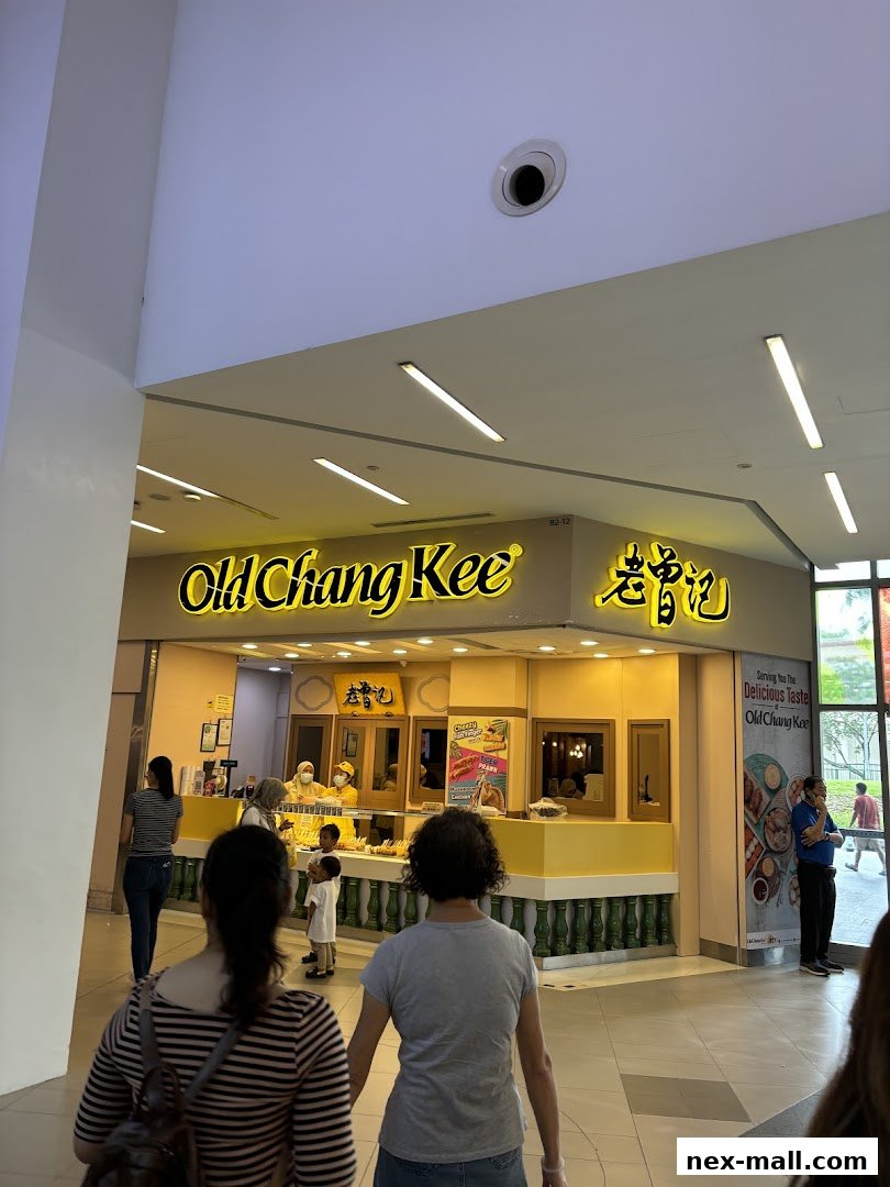 People walking towards the brightly lit Old Chang Kee shop with its signature yellow signage.