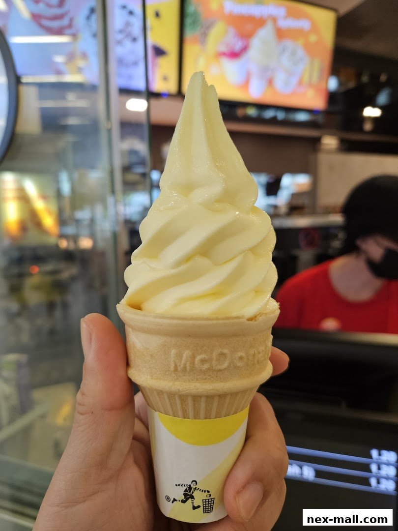 A hand holds a McDonald's soft-serve ice cream cone with a pineapple swirl.