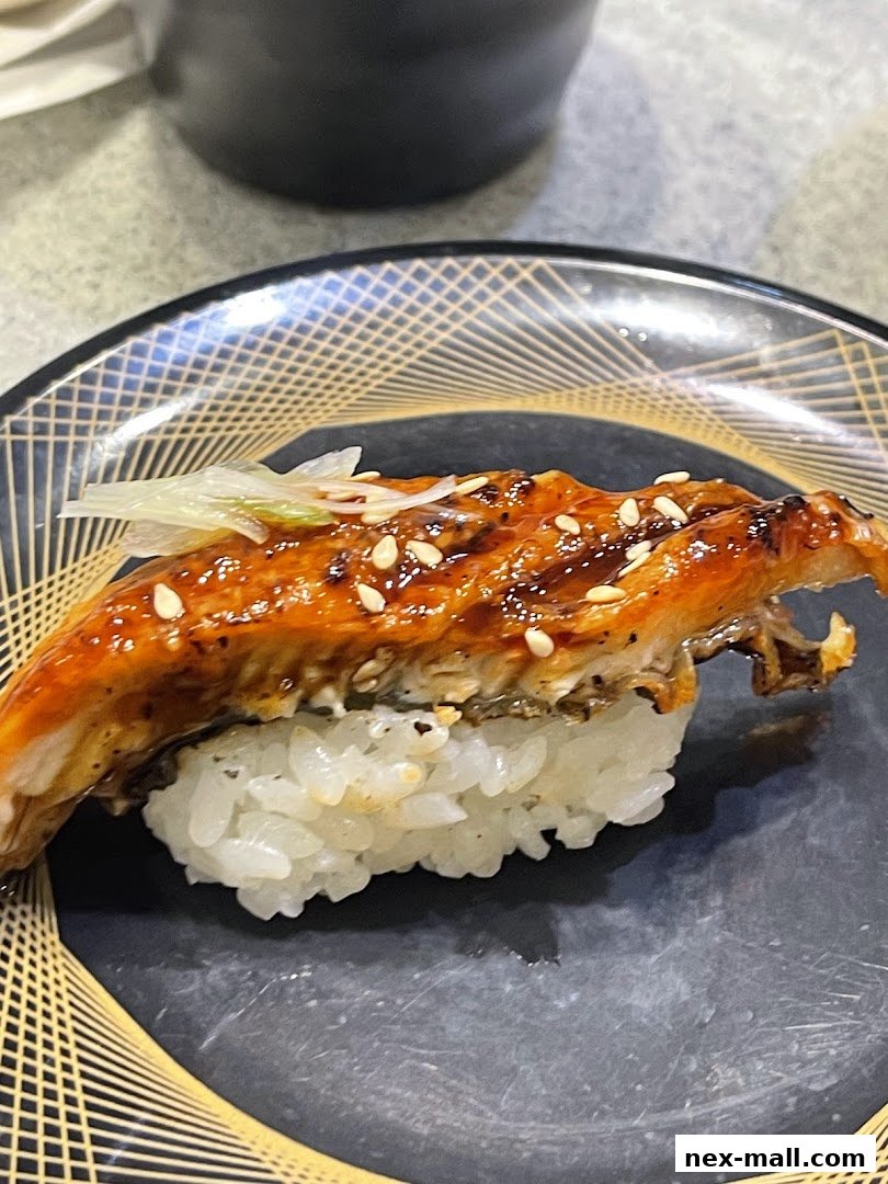 A close-up of a delicious piece of grilled eel sushi on a black plate.