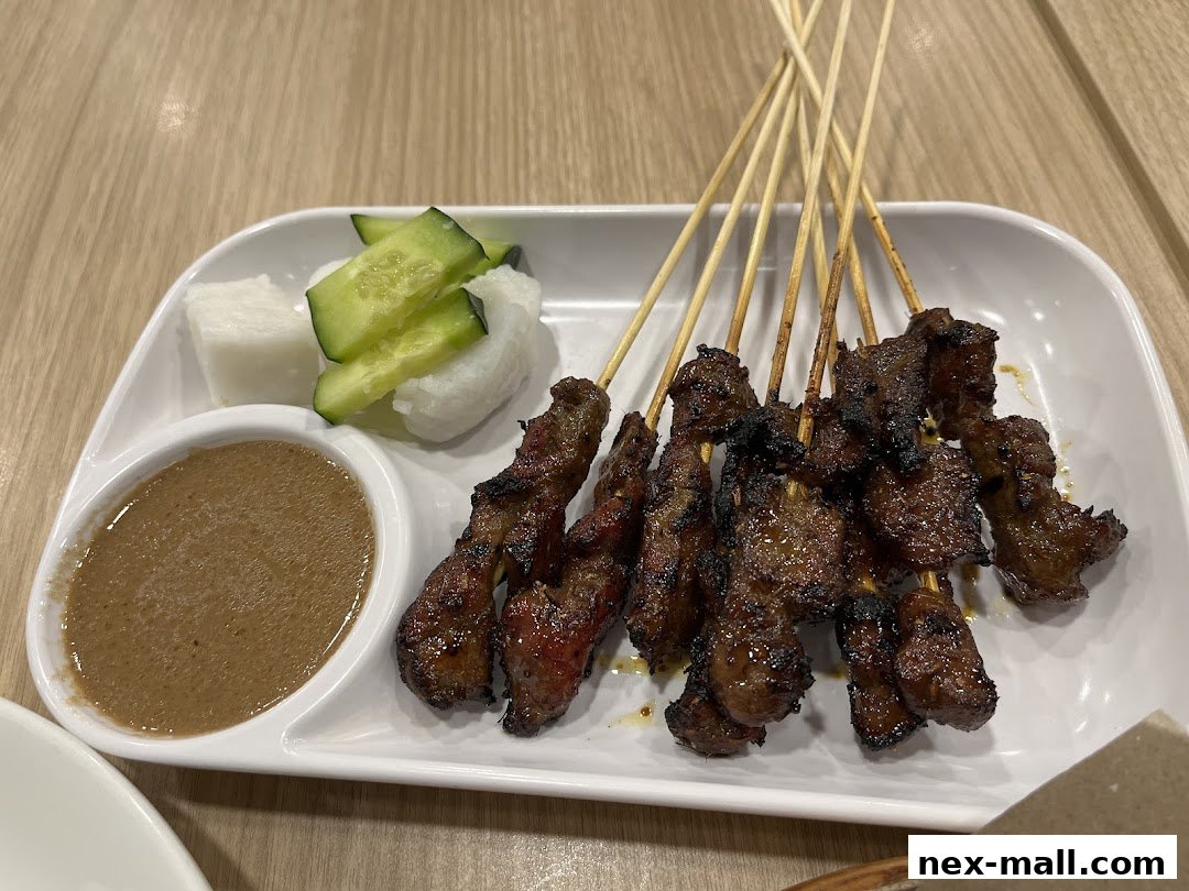 A plate of grilled satay skewers with peanut sauce, rice cakes, and cucumber slices.
