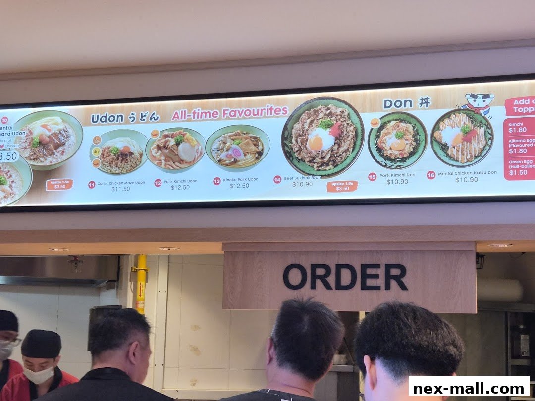 A brightly lit menu board displaying various Udon and Donburi dishes with prices.