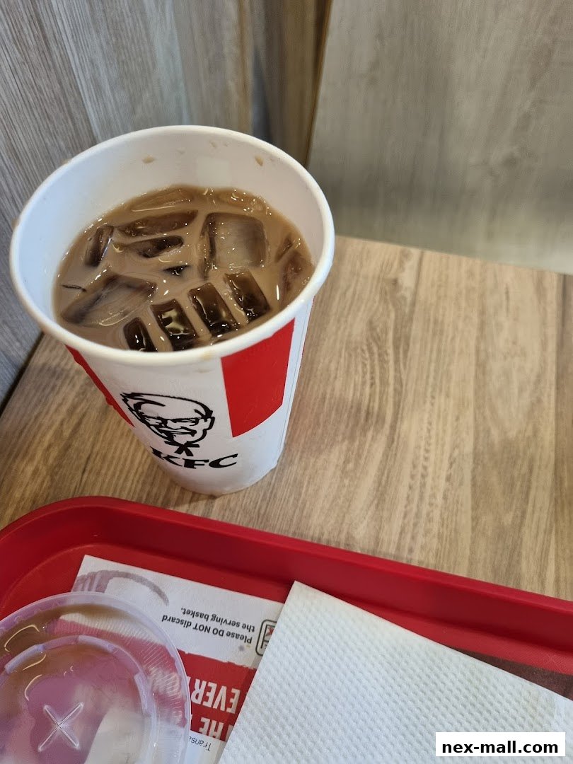 A close-up of a KFC branded cup filled with iced coffee on a red tray.