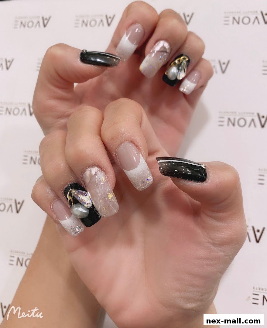 A close-up of a hand showcasing elaborate nail art with French tips, glitter, and 3D embellishments.