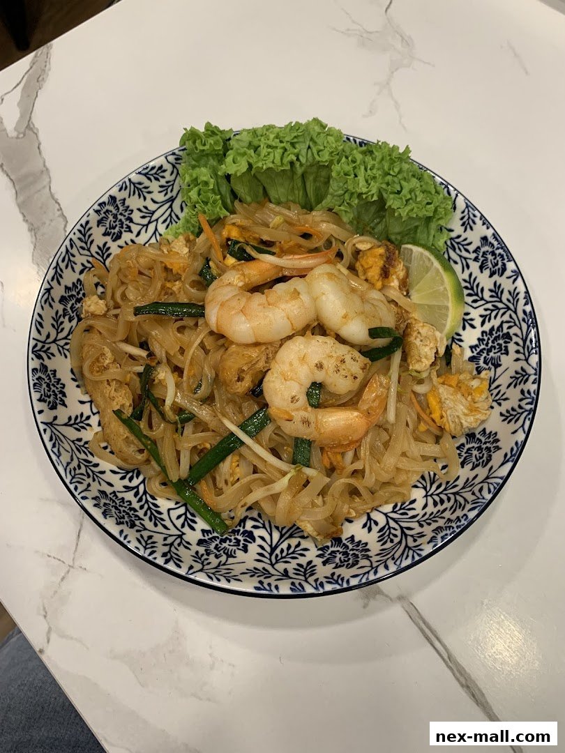 A plate of Pad Thai with shrimp, lettuce, and lime on a marble table.