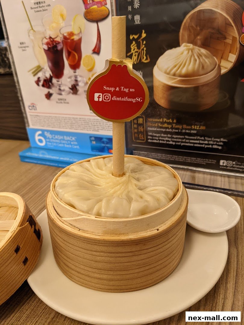 A close-up of a steaming basket of soup dumplings with a promotional sign.