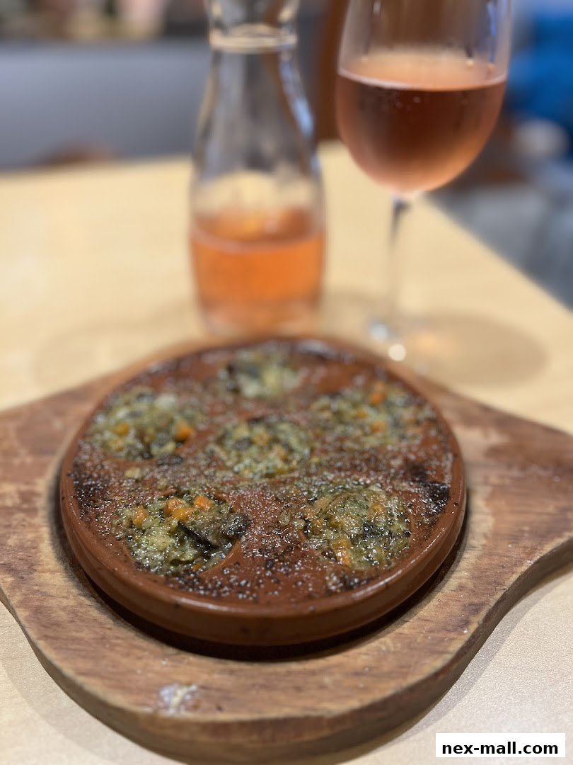 A dish of escargots served with a glass of rosé wine and a small carafe of wine.