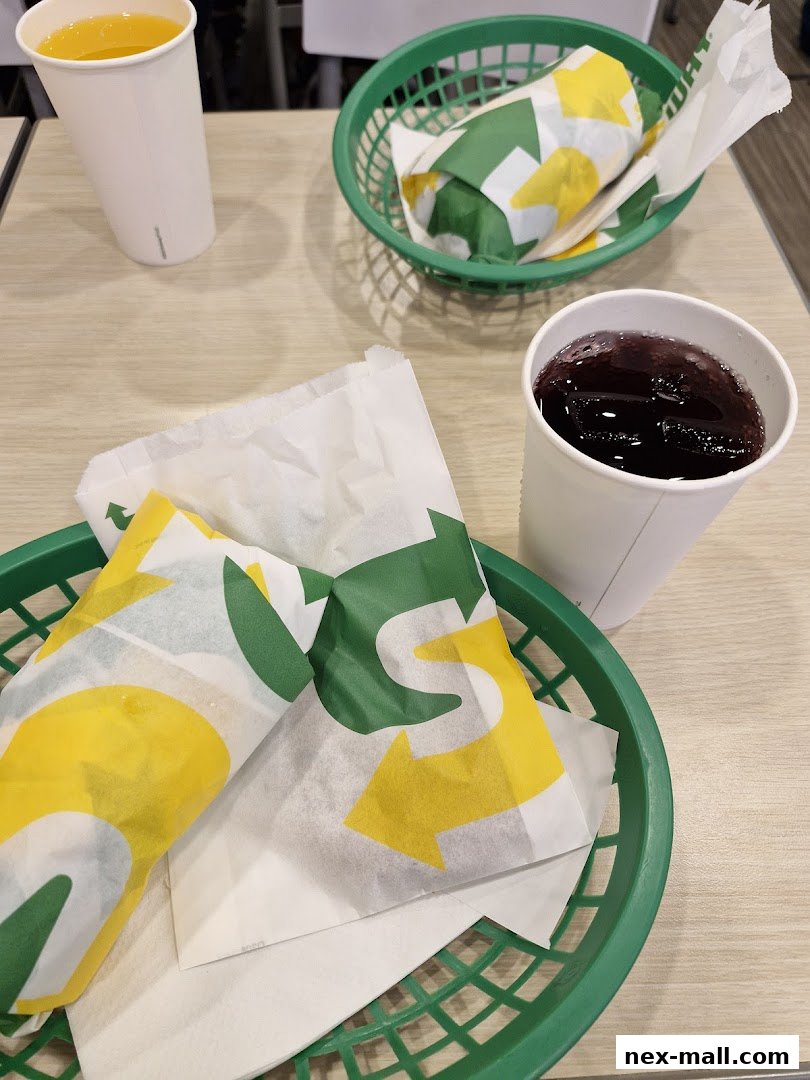 Two Subway sandwiches and drinks served in green baskets on a table.