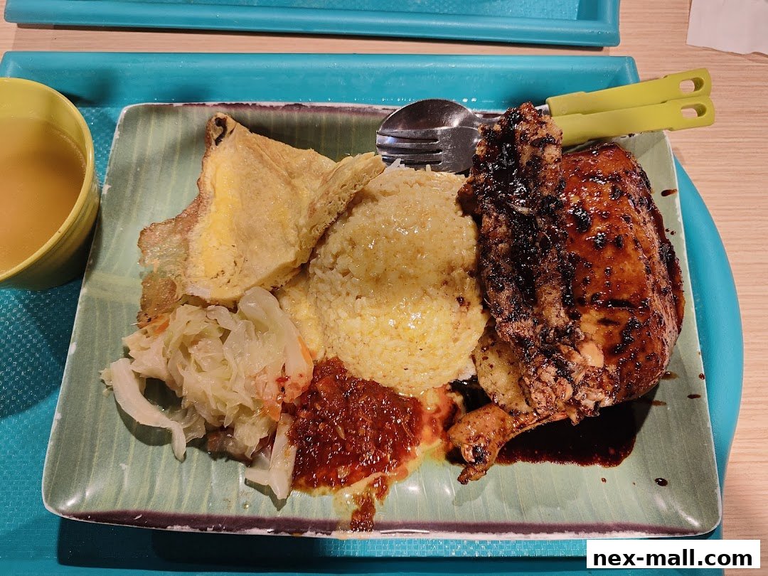 A plate of chicken rice with omelette, braised cabbage, and chili sauce, served with soup.