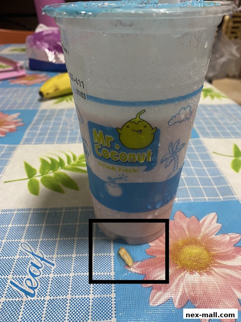 A cup of Mr. Coconut drink with a straw and a banana in the background.