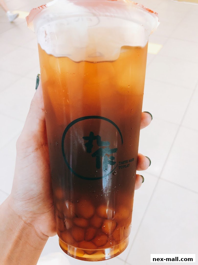 A hand holds a large bubble tea with a creamy foam topping and brown tapioca pearls.