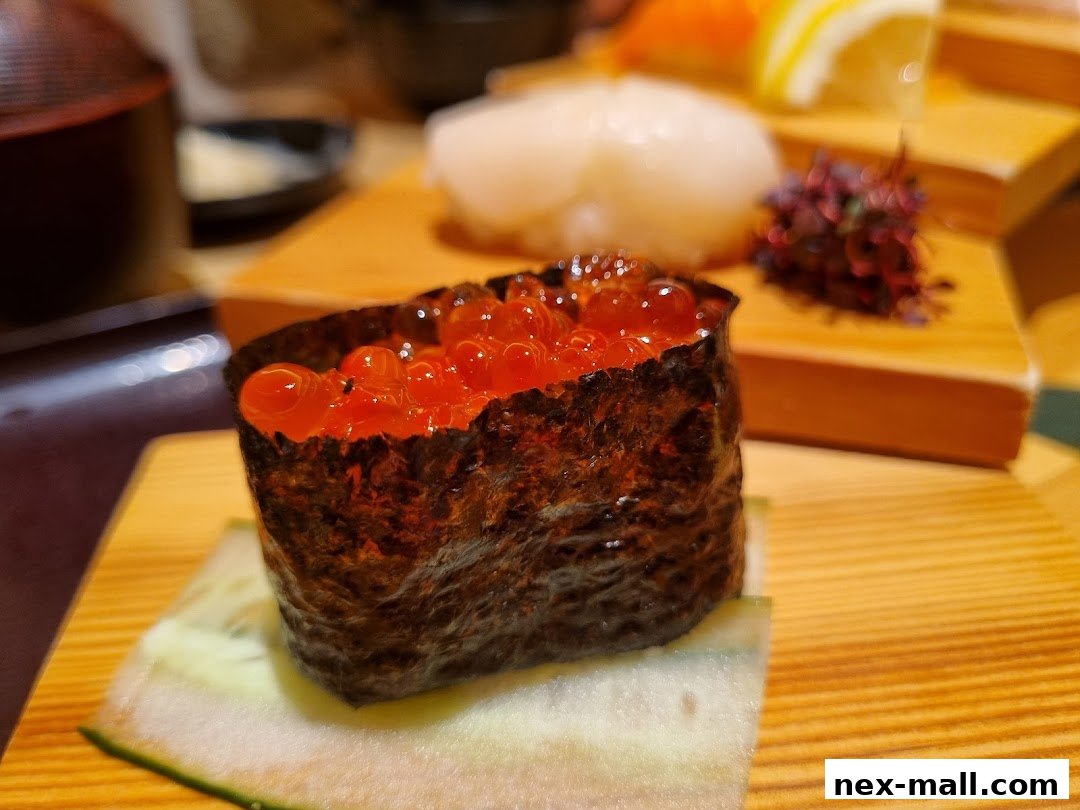 A close-up of ikura (salmon roe) sushi on a wooden board with other sushi in the background.
