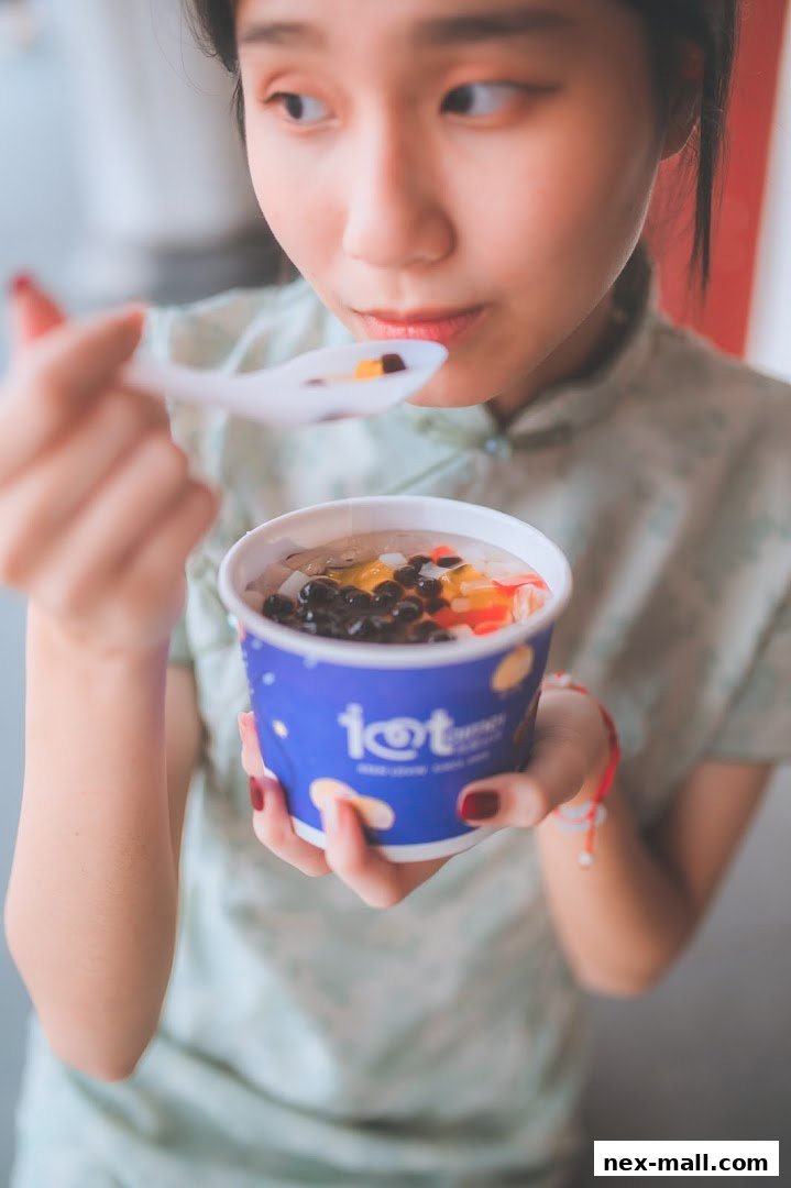 A young woman enjoys a colorful dessert with tapioca pearls and fruit from a blue cup.