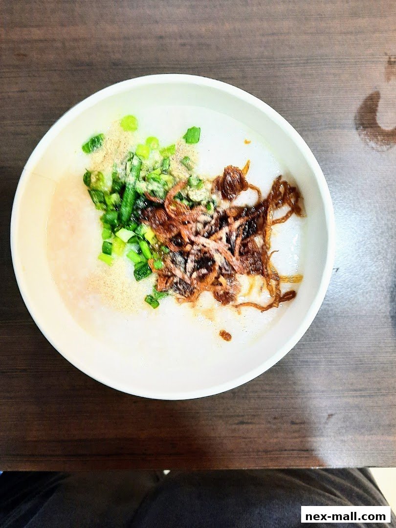 A bowl of congee topped with scallions, fried shallots, and a sprinkle of seasoning.