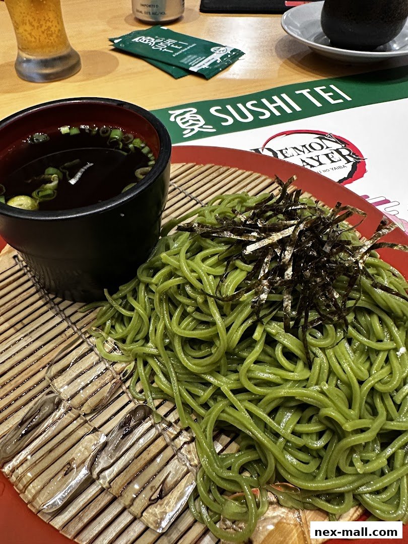 A plate of green soba noodles with a side of broth and a glass of beer.