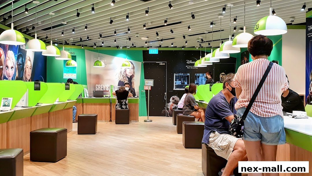 Customers are being served at counters in a brightly lit telecommunications store with digital displays.