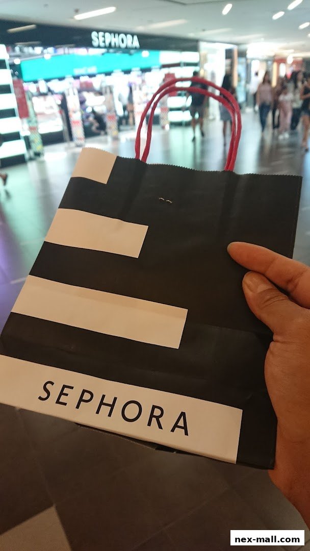 A hand holds a Sephora shopping bag in front of the store.