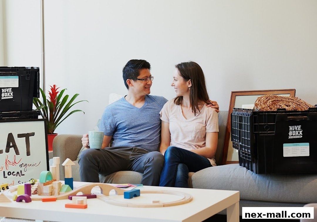 A couple sits on a couch surrounded by moving boxes and children's toys.
