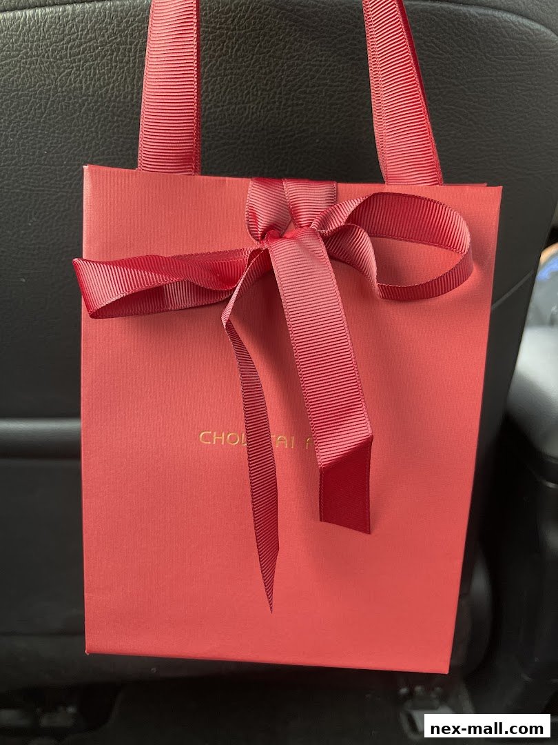 A red gift bag with a red ribbon bow and handles, featuring gold lettering.
