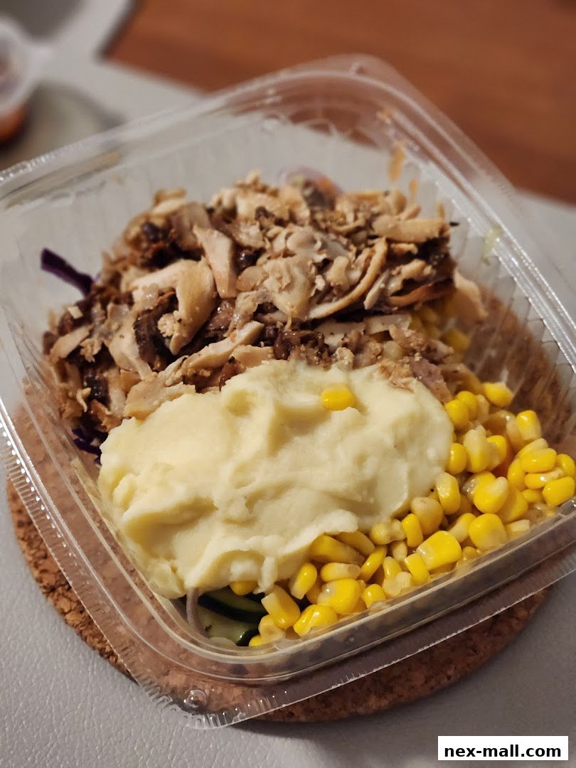 A clear plastic container filled with a meal featuring shredded chicken, mashed potatoes, and corn.