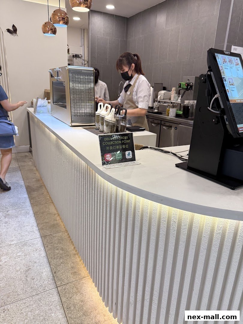 A staff member serves customers at the counter of a modern bubble tea shop.