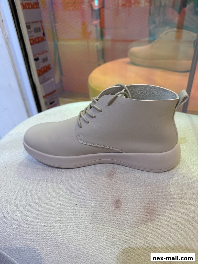 A light beige leather shoe with laces is displayed on a textured surface.
