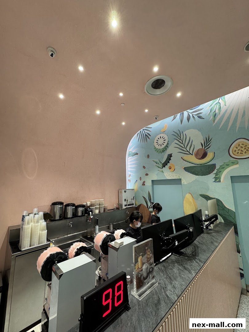 Two staff members work behind a counter at Fruce NEX, with a vibrant fruit-themed mural on the wall.