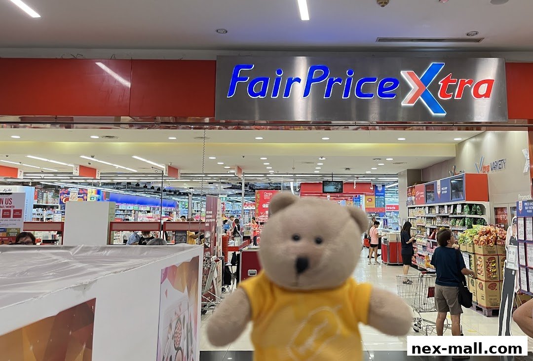 A teddy bear in a yellow shirt stands in front of the FairPrice Xtra supermarket entrance.