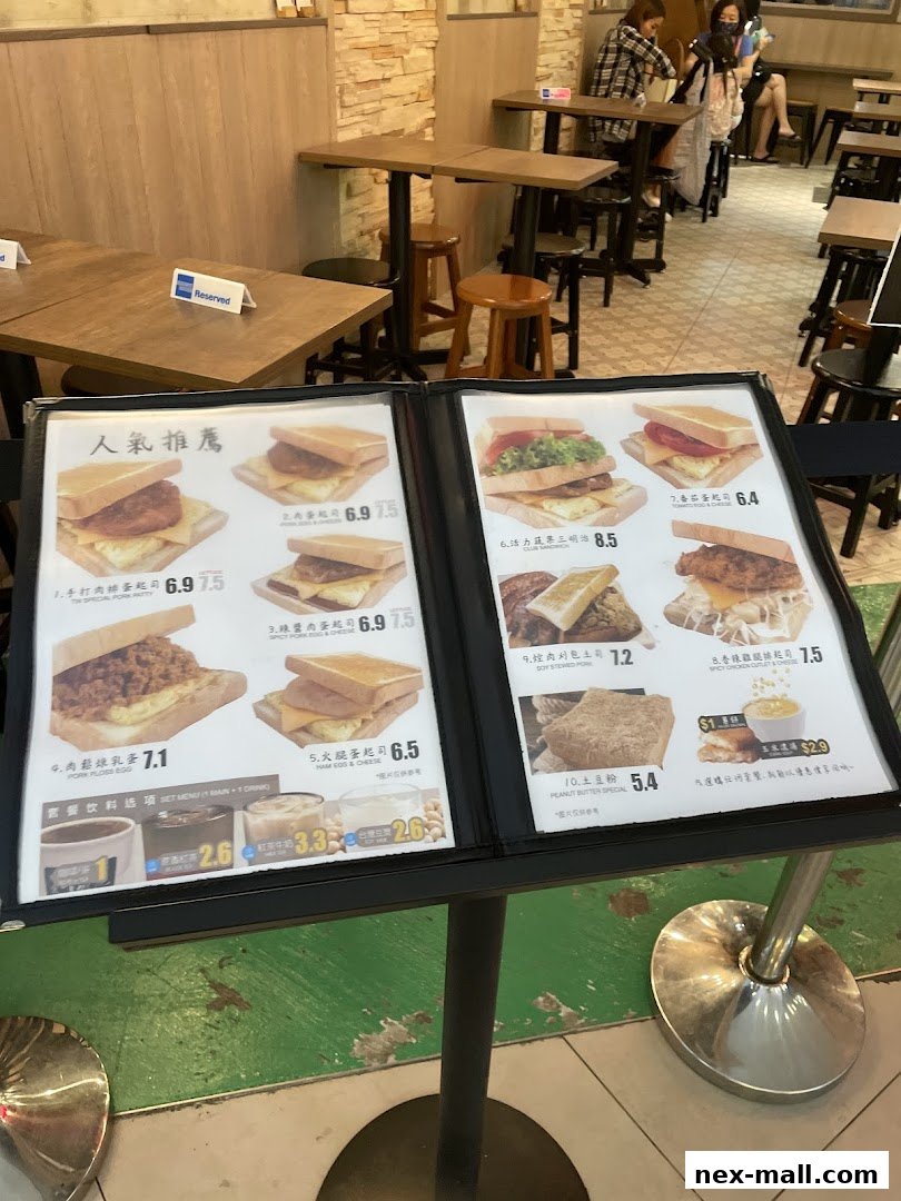 A menu displaying various sandwiches and drinks with prices, set on a stand inside a cafe.
