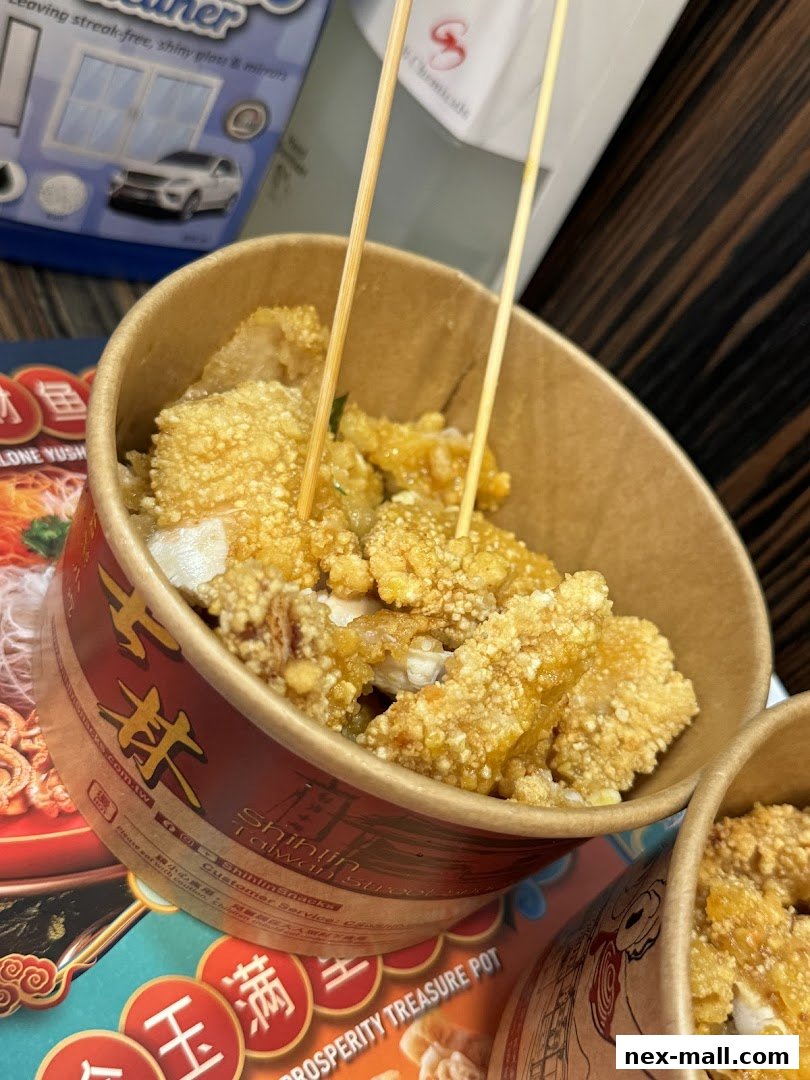 A close-up of crispy fried chicken pieces served in a paper bowl with skewers.