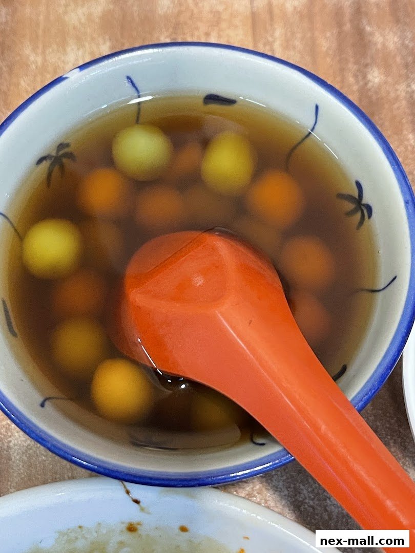 A close-up shot of a bowl of sweet soup with small, round dumplings and an orange spoon.