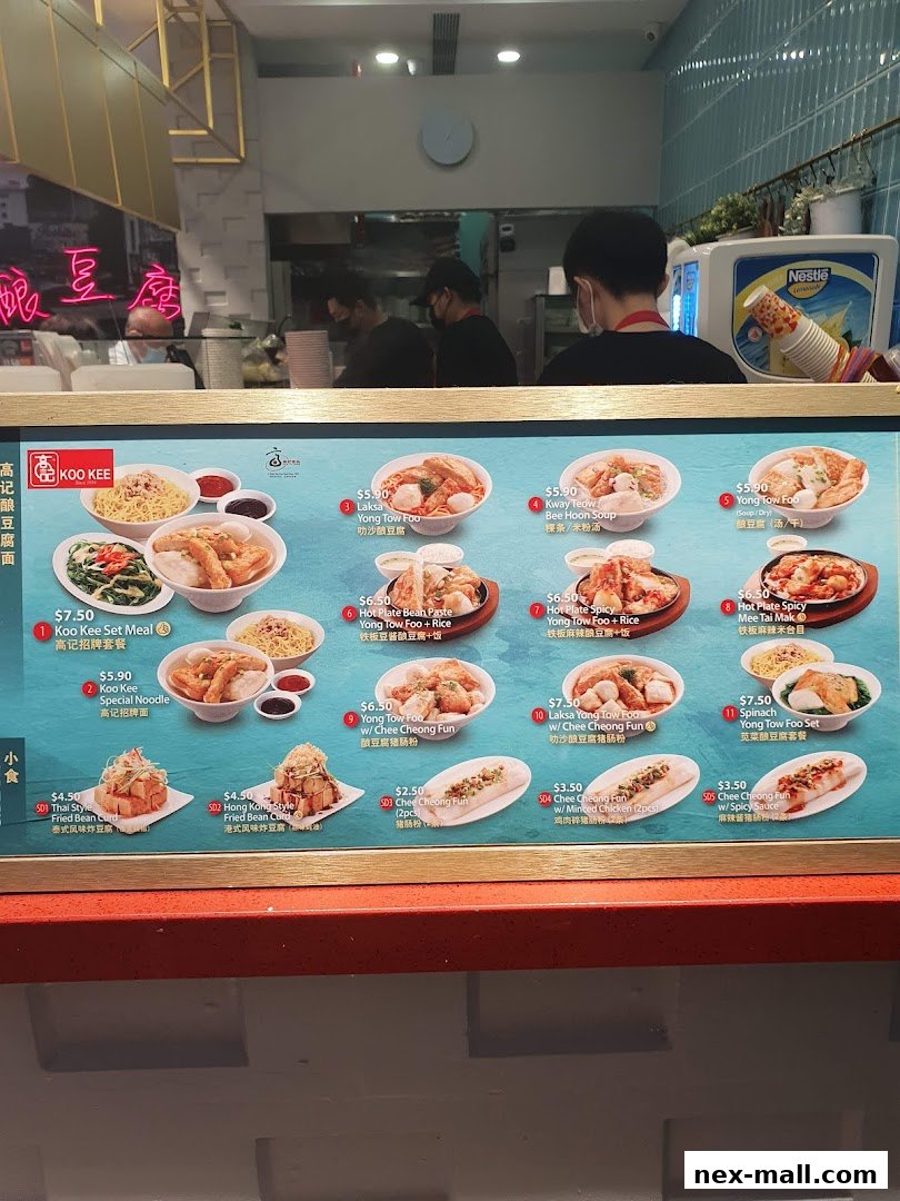 A menu board for Koo Kee restaurant showcasing various noodle and bean curd dishes with prices.