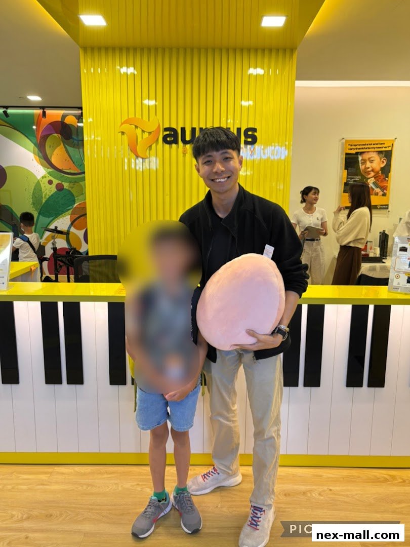 A smiling man and a child stand in front of a bright yellow wall with the Aureus Academy logo.