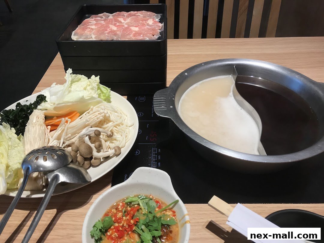 A shabu-shabu meal with thinly sliced meat, assorted vegetables, and a split broth pot.