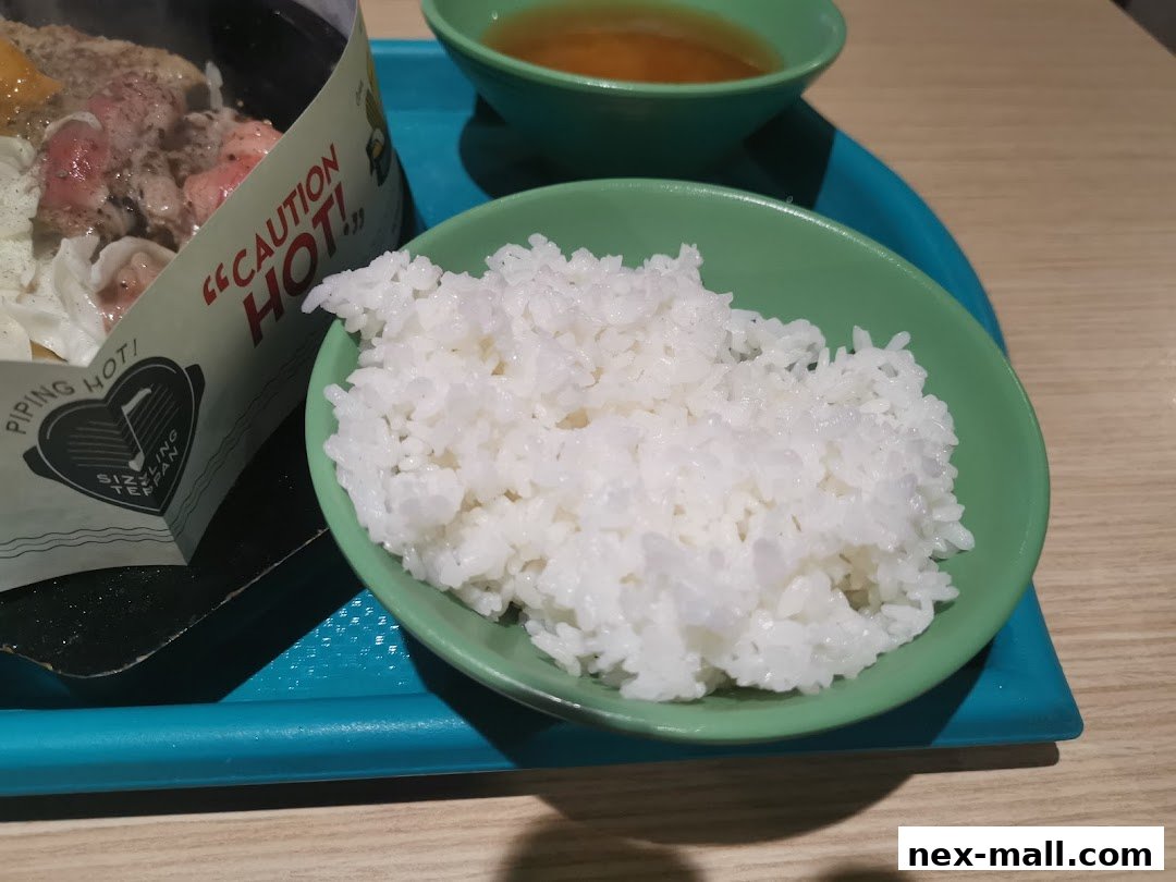 A close-up of a steaming bowl of white rice next to a sizzling plate with meat and vegetables.
