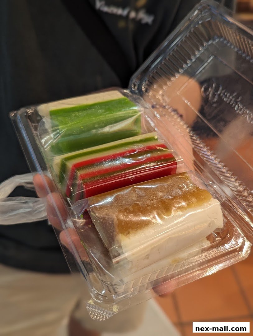 A person holds a clear plastic container filled with colorful layered desserts.