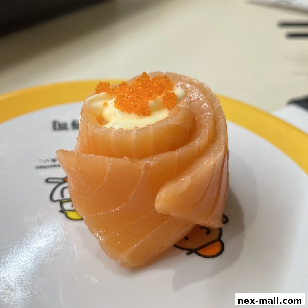 A close-up of a salmon sushi roll topped with mayonnaise and tobiko on a white plate.