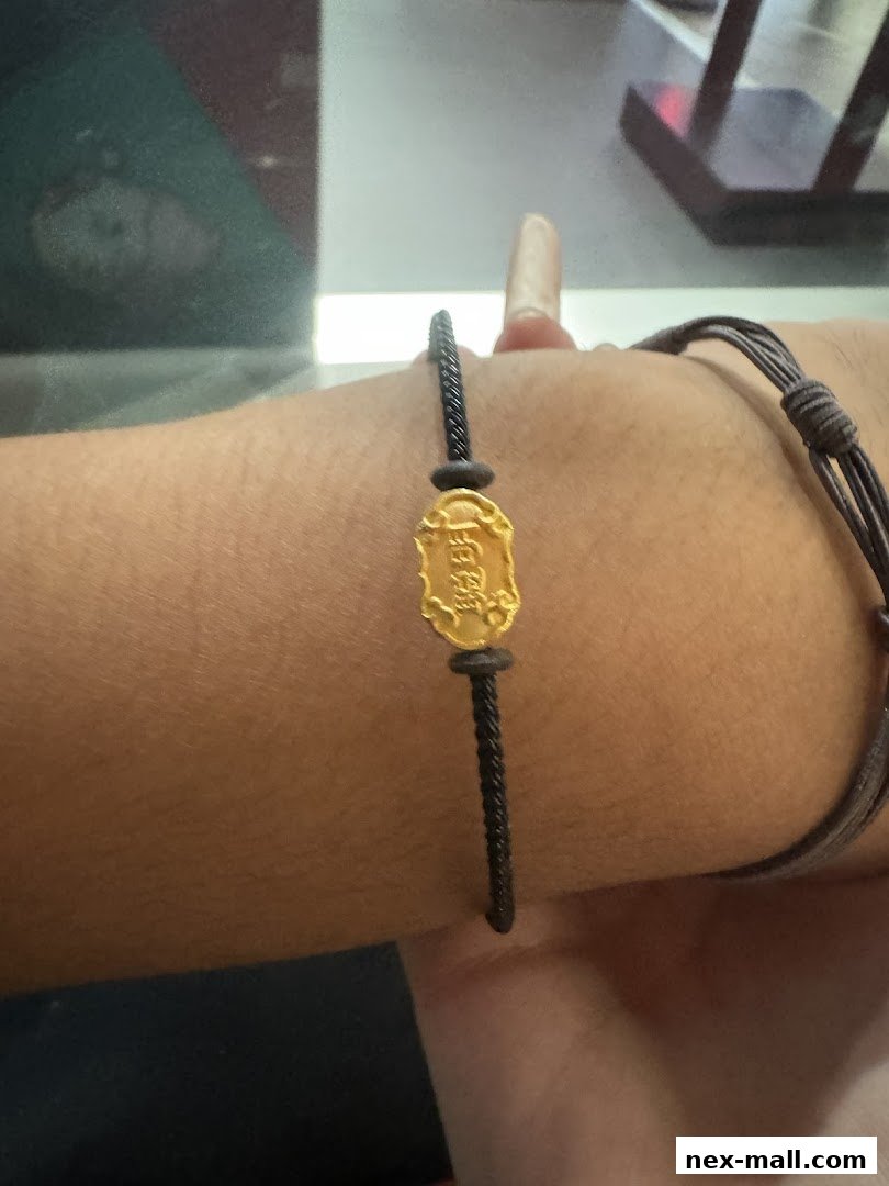 A close-up shot of a person's arm wearing a gold charm bracelet with a black cord.