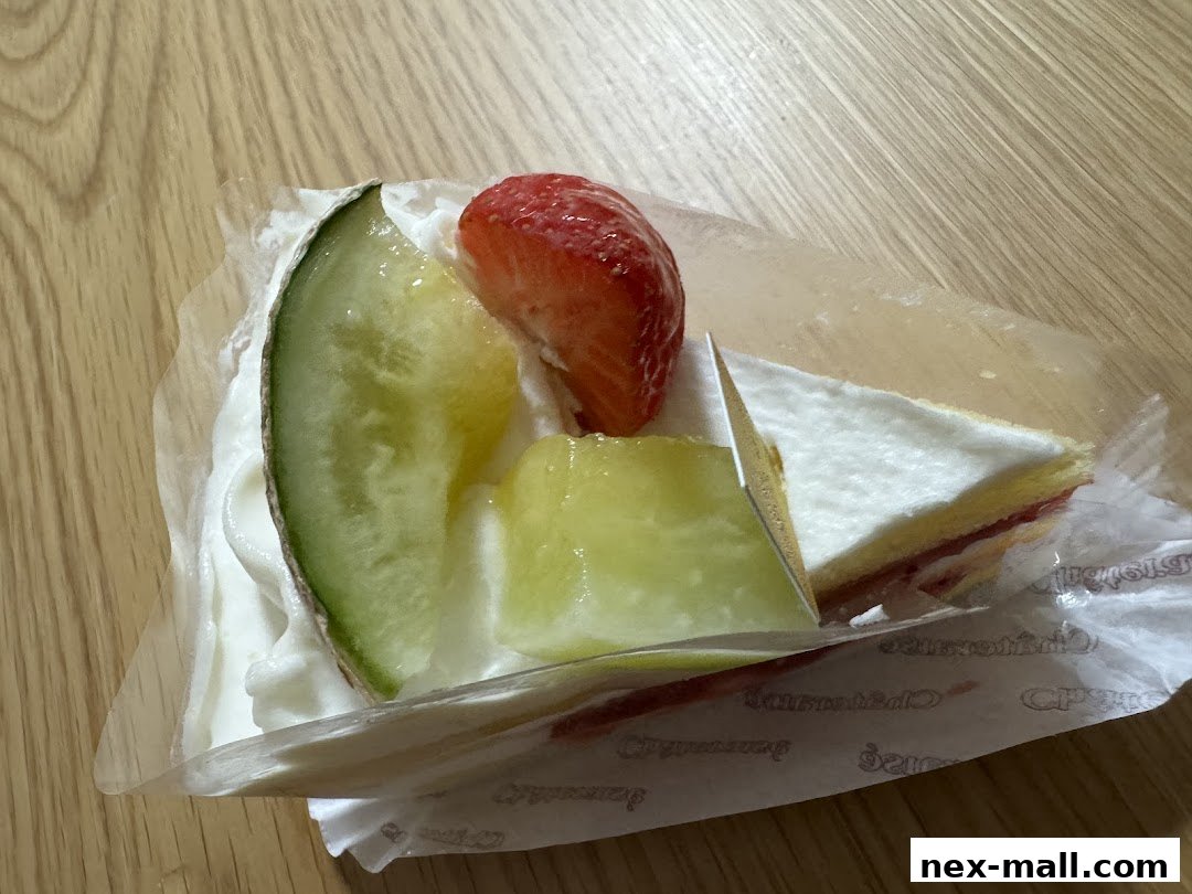 A slice of cake with whipped cream, melon, and strawberry on a wooden surface.