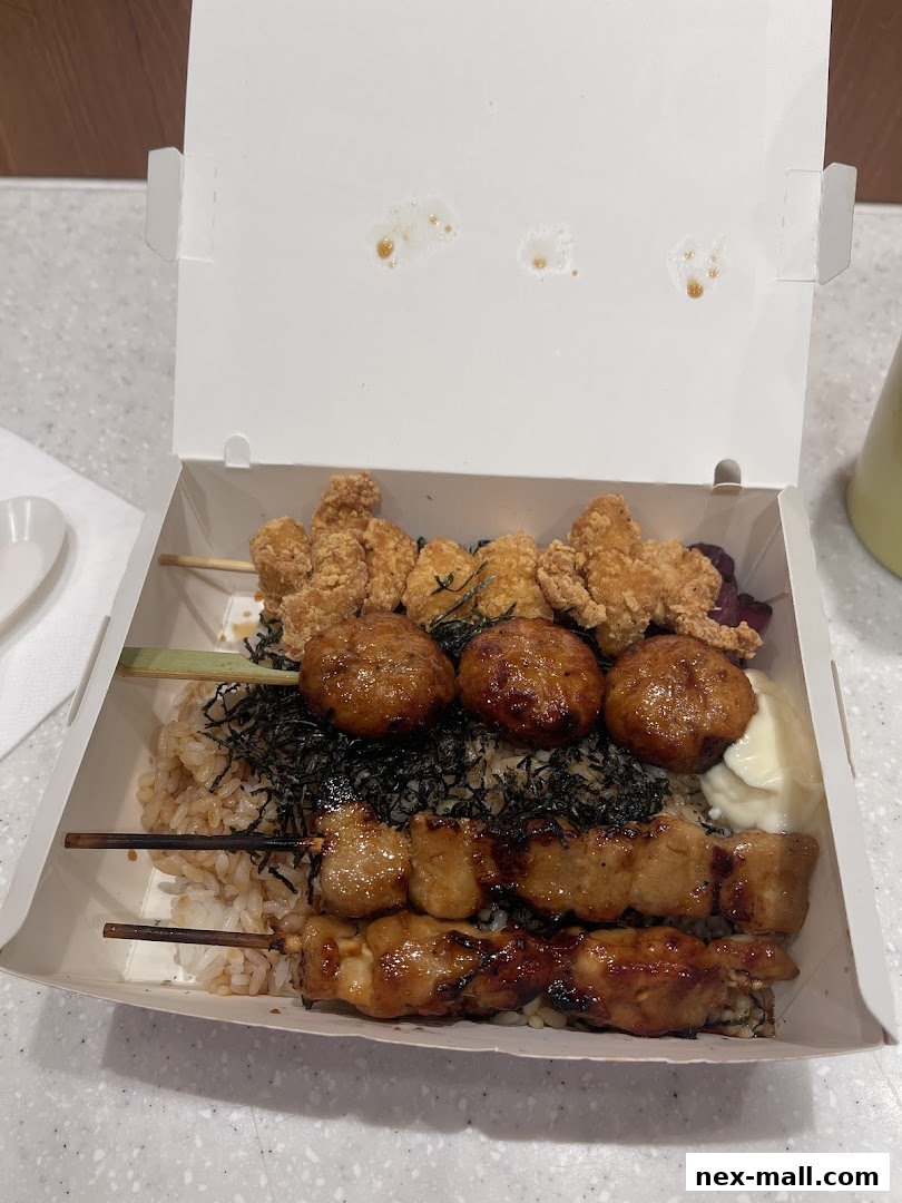 A takeout box filled with rice, chicken skewers, and fried chicken pieces.