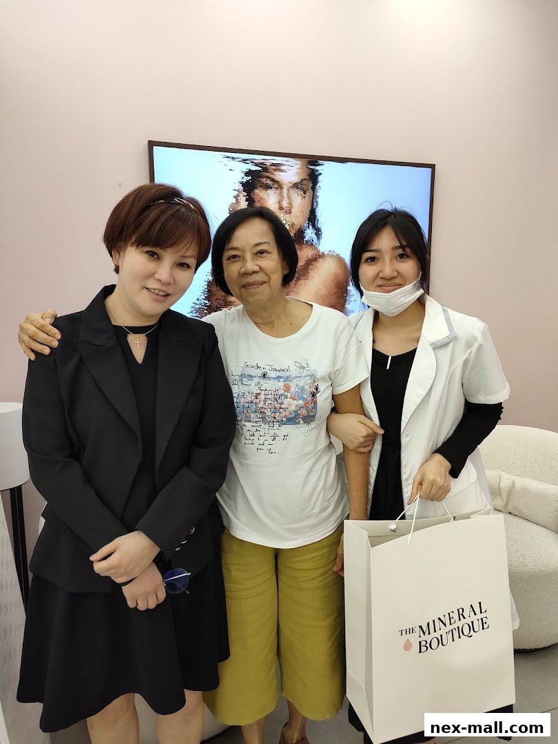 Three women smiling in front of a large screen displaying an artistic image, one holding a shopping bag.