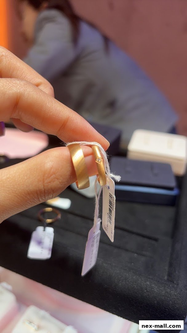 A person holds two gold rings, one with a small diamond, in front of a jewelry display.