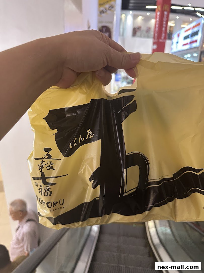 A hand holds a yellow shopping bag from Gokoku Japanese Bakery.