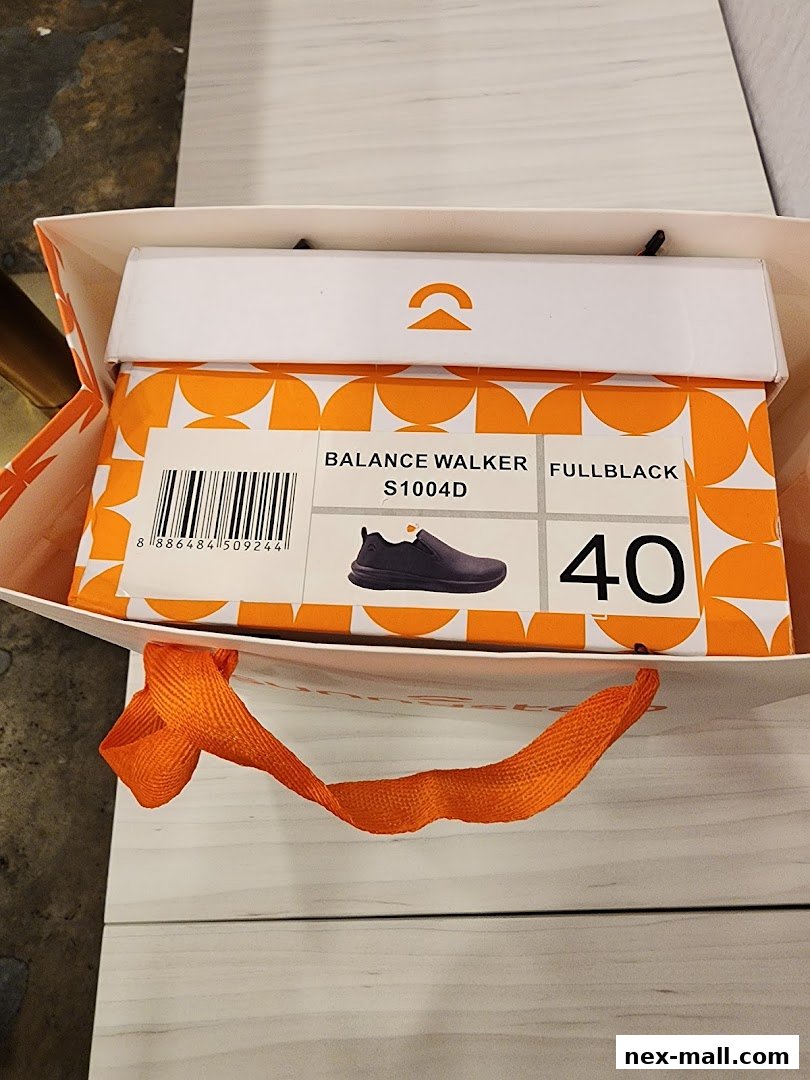 A shopping bag with a shoe box inside, showing a pair of black slip-on shoes.
