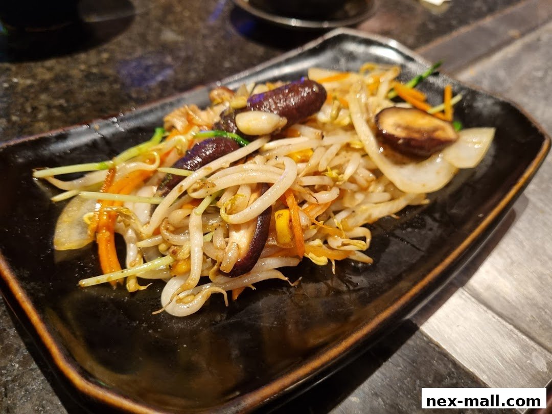 A close-up of a stir-fried vegetable dish with bean sprouts, mushrooms, carrots, and onions.
