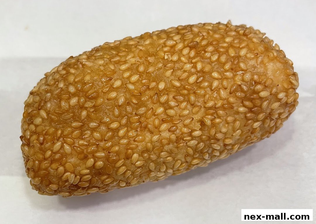 A close-up shot of a golden-brown, oval-shaped pastry covered in sesame seeds.