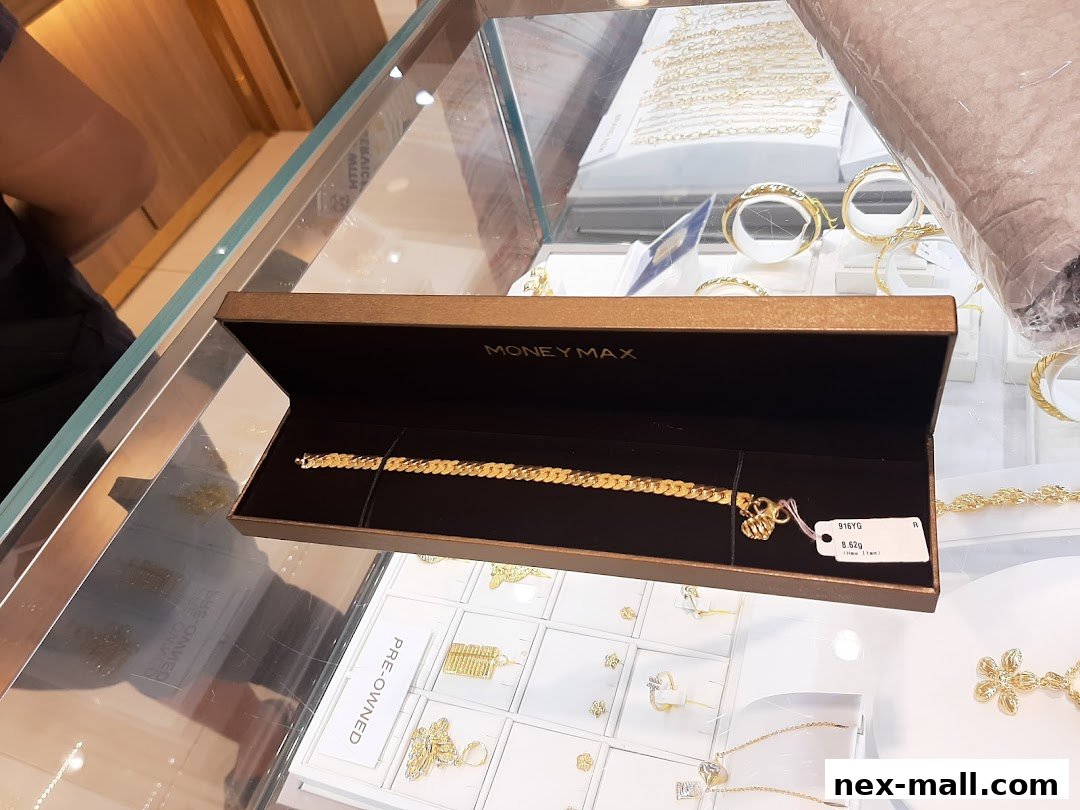 A gold bracelet displayed in a box at MoneyMax Pawnshop, with other jewelry visible in the background.