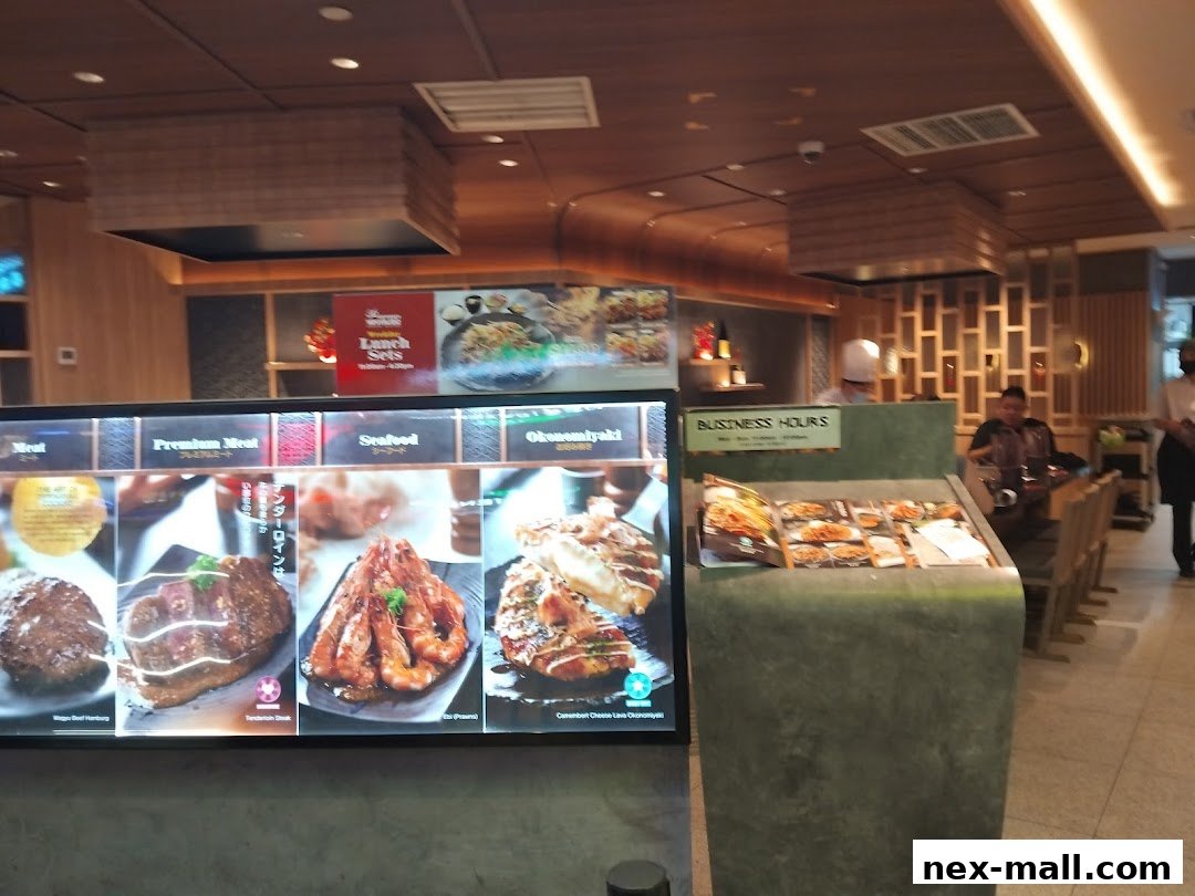 A digital menu board displays various Japanese dishes, with a business hours sign and dining area in the background.
