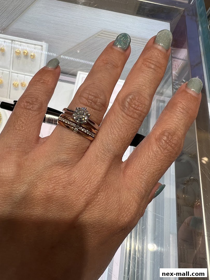 A hand with rings and glittery nails is shown in front of a display of jewelry.